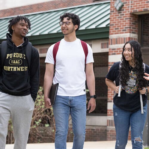 Three students walk down a sidewalk