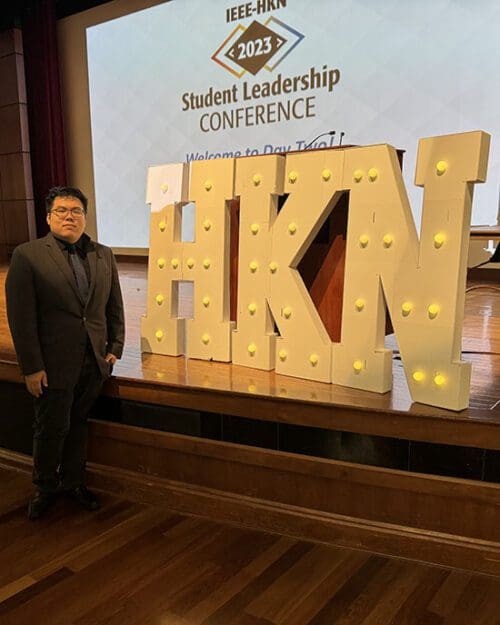 A PNW Student stands next to a marquee sign reading "HKN"