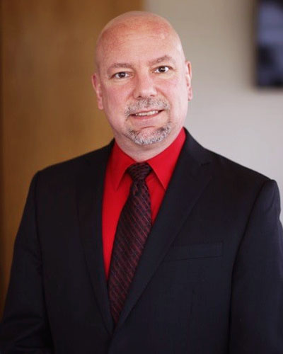 Professional photo of Mason Macenski in a red shirt and black suit and tie.