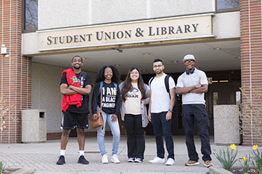 Five students stand together outside of the Student Union Library Building