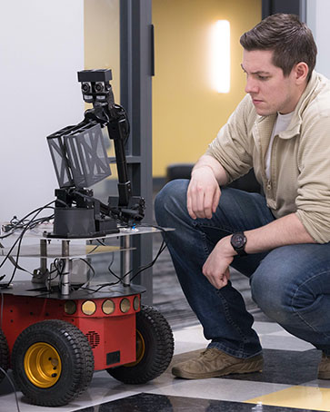 A student kneels next to a robot