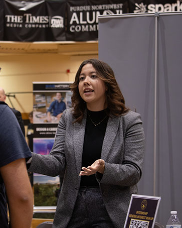 A College of Business alumni stands in a suit jacket and talks to current students.