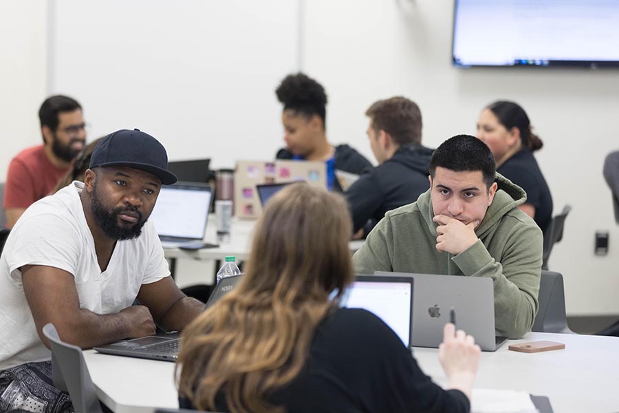 Students sit at round desks in a classroom.