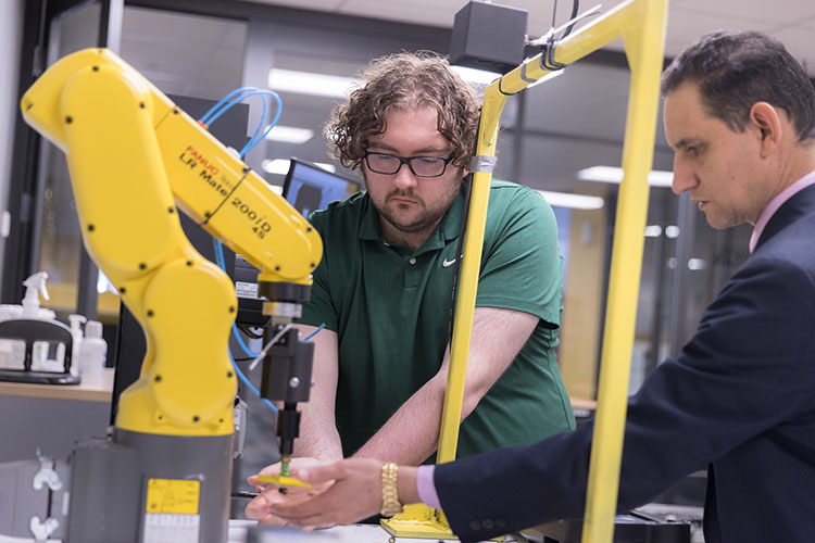 A professor and student work on a robotic machine