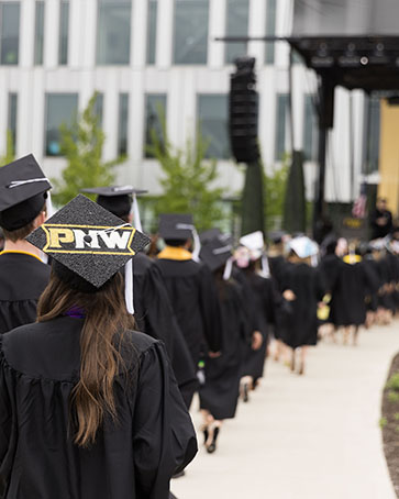 PNW graduates in the procession at spring 2023 commencement. A mortar board decorated with PNW is visible, as is the Nils K. Nelson Bioscience Innovation Building in the background.