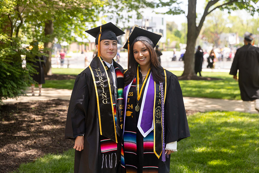 Two students stand together in their commencement regalia.