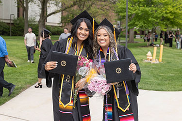 Two students pose with their degrees during a commencement ceremony