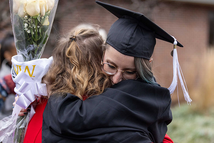 A PNW graduate with flowers hugs a loved one