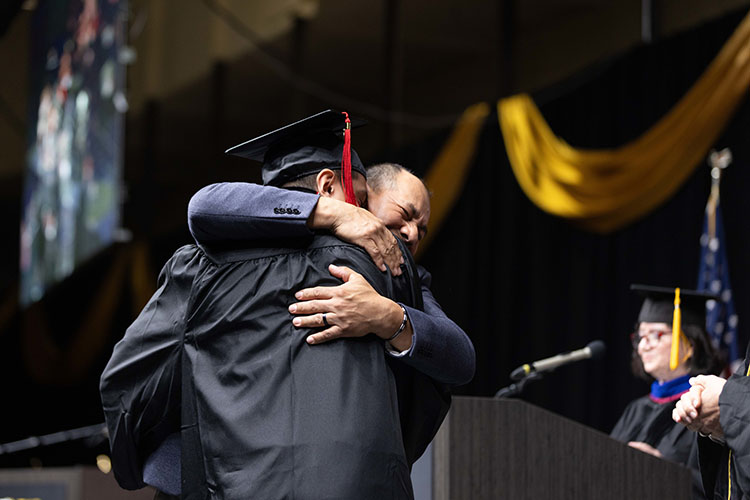 A PNW graduate embraces someone on stage