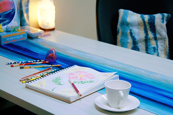 A sketch book, colored pencils and a coffee cup sit on a table