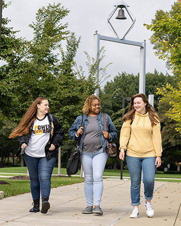 Three students walk together outside with the PNW Bell Tower in the background