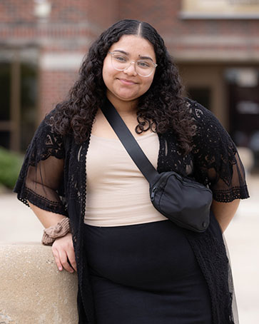 A student stands outside and leans against a concrete structure