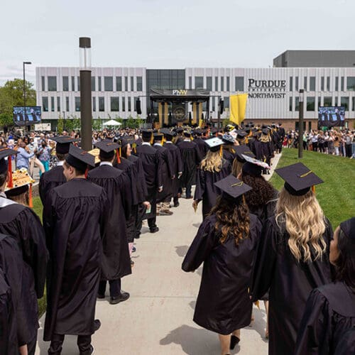 PNW graduates in regalia walk to the Nils K. Nelson Bioscience Innovation Building.