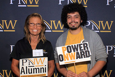 PNW alumni pose together with "PNW Alumni" and "Power Onward" signs at a campus event.