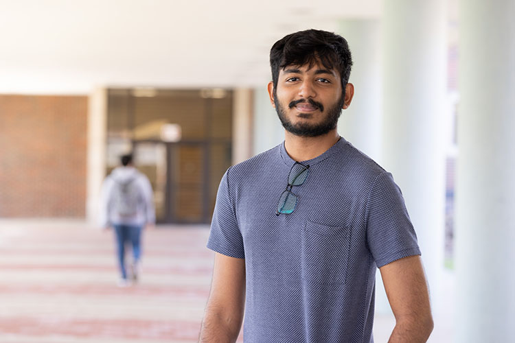 A graduate student stands in a blue short sleeve t-shirt