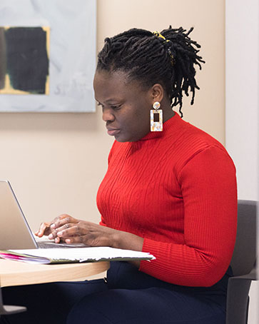 A graduate student in a red long sleeve shirt sits at a table and works on a computer