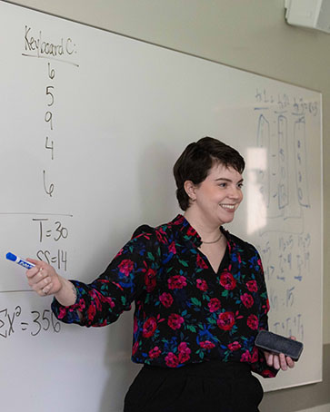 Abigail Dempsey stands in front of a white board while teaching