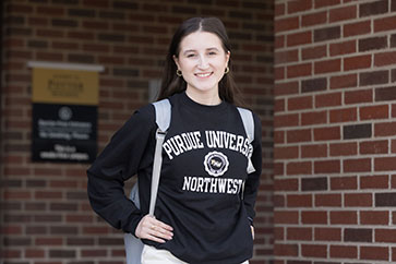 A student in a black PNW sweatshirt and backpack smiles at the camera.