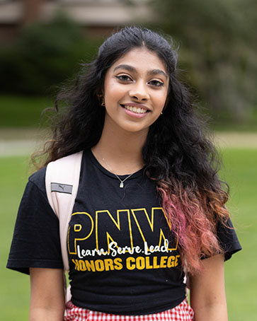 A student in an honors college shirt stands alone and smiles