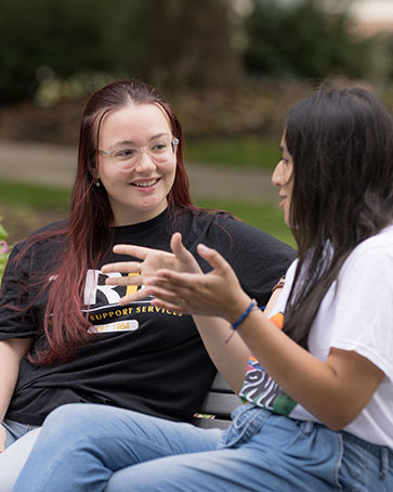 Two students sit on a bench and talk