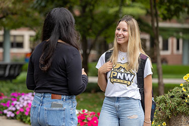 Two students stand outside and talk to each other