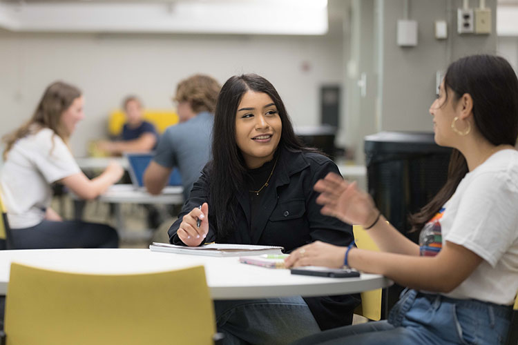 One student is in focus - there are several students in the room, all sitting at white, round tables.