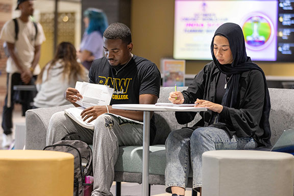 Two students sit in the Mane Zone and look at papers