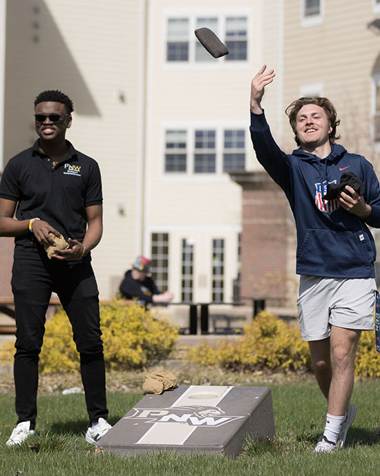 Two students play bean-bag toss outside