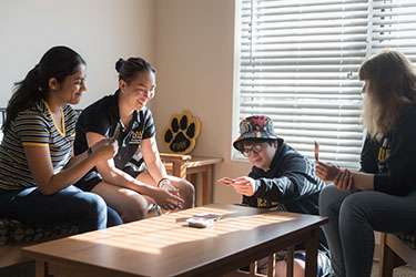 Four students sit around a table in a dorm and play Uno