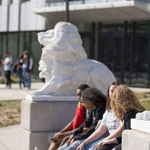 PNW students sit by a lion sculpture in front of the Nils K. Nelson Bioscience Innovation Building