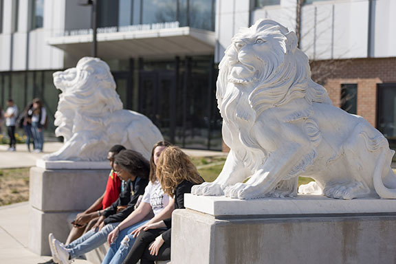 PNW students sit by a lion sculpture in front of the Nils K. Nelson Bioscience Innovation Building