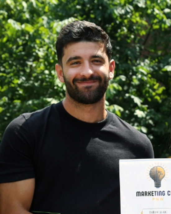 A PNW student stands outdoors holding a certificate