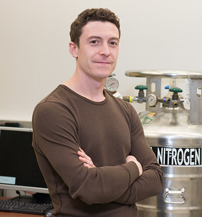 Brian Murphy stands with his arms crossed in front of nitrogen container