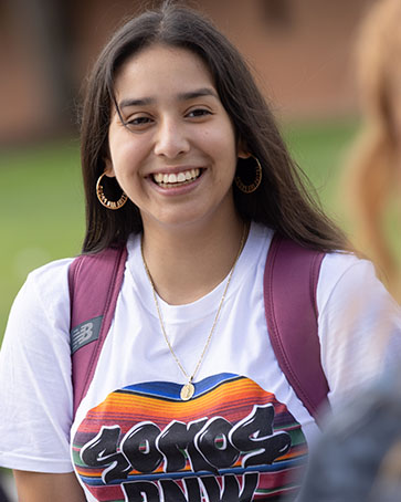 A student in a white Somos PNW shirt and long brown hair smiles.