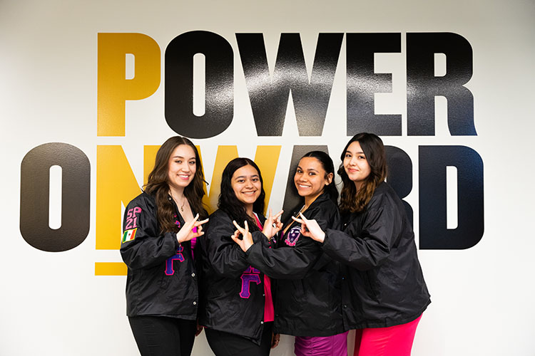 Four PNW students, also members of the Sigma Lambda Gamma National Sorority, pose for a phone together, making their sorority sign with their hands.