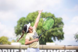 A player on the PNW women's tennis team throws a tennis ball in the air and holds a racket in the other hand