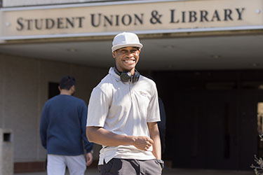 A PNW student stands in front of the Student Union & Library Building