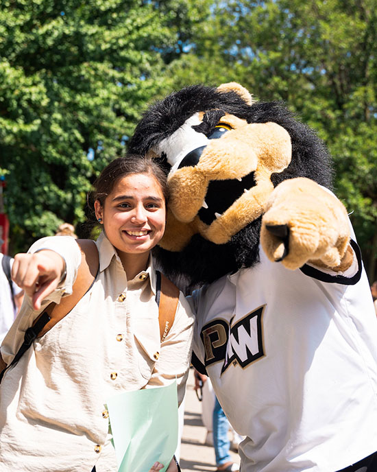 A PNW student and mascot Leo point at the camera at a Welcome Rally.