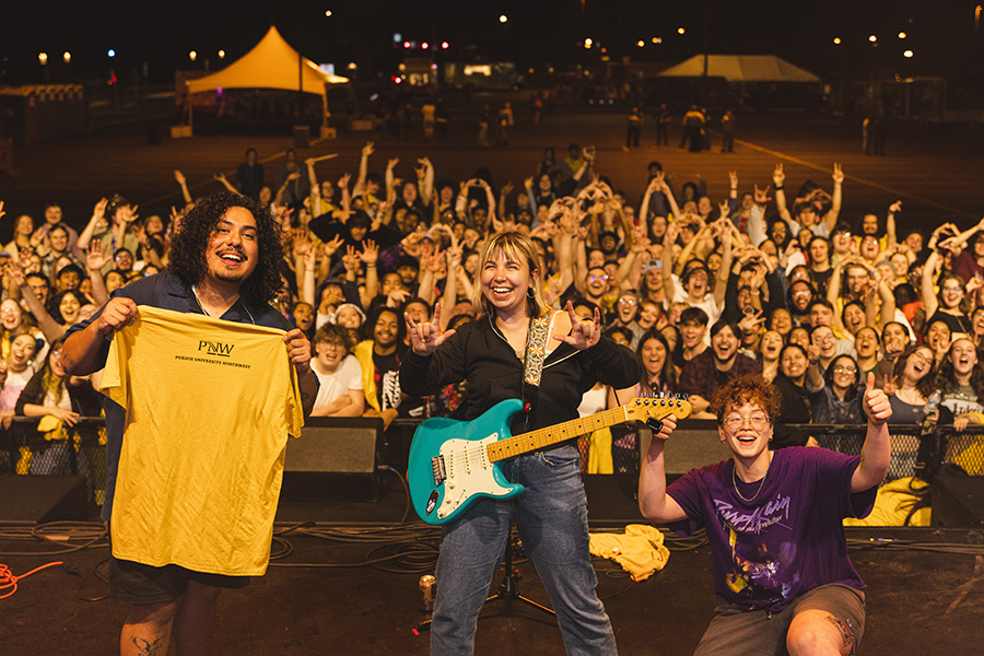 Beach Bunny band poses on stage while PNW Students are in the background.