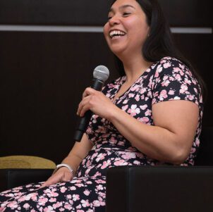 Sandra Patino (MA’19) sits on stage holding a microphone.