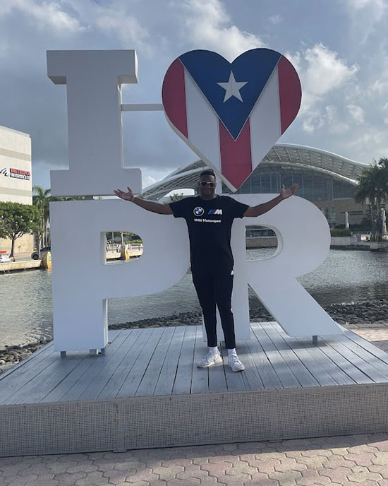 Khalil Hudson stands in front of a sign that reads "I [heart symbol] PR" sign.