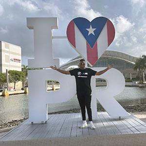 Khalil Hudson stands in front of a sign that reads "I [heart symbol] PR" sign.