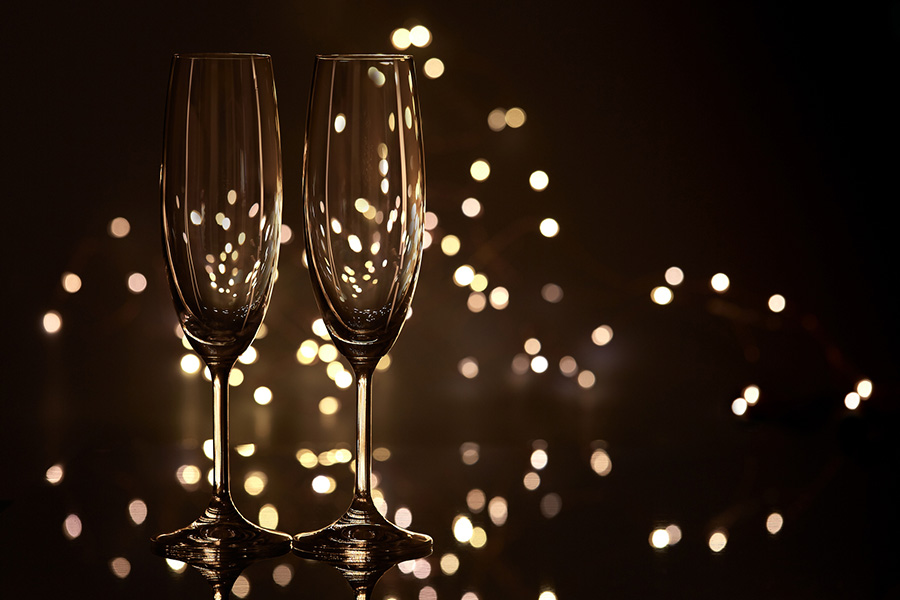 Two empty glasses for champagne on a dark background with LED lights garland. Copy space for text.