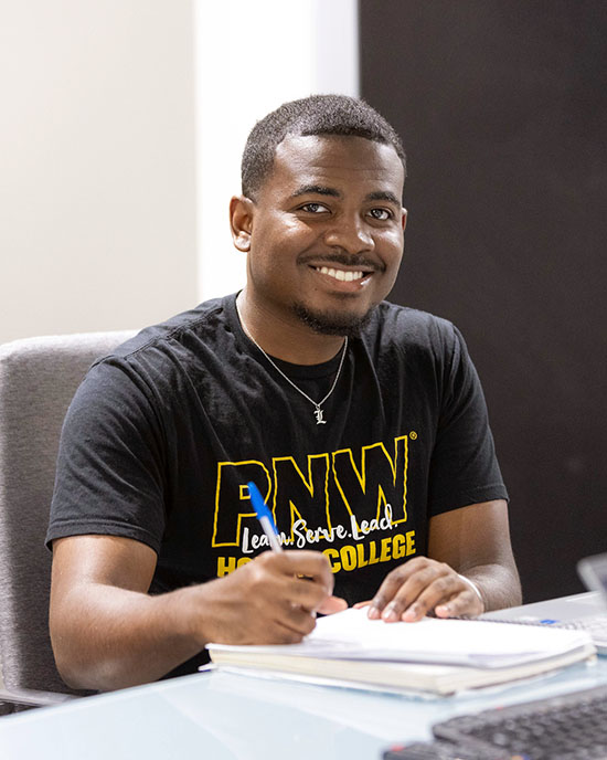 A male student in a PNW t-shirt works at a desk