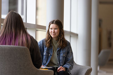 A student in a jean jacket and green shirt sits in front of windows