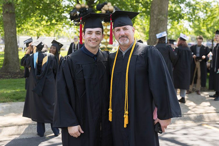Jacob Wheeler Sr. and Jacob Wheeler Jr. stand together in commencement regalia.