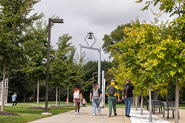 Pictured is an image of the Hammond Bell Tower in the distance with students walking along the sidewalk