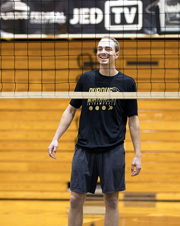 A PNW student stands behind a volleyball net