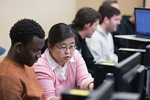 Students sit at desktop computers and collaborate