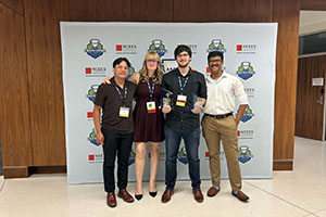 Four students stand together in front of a photo backdrop